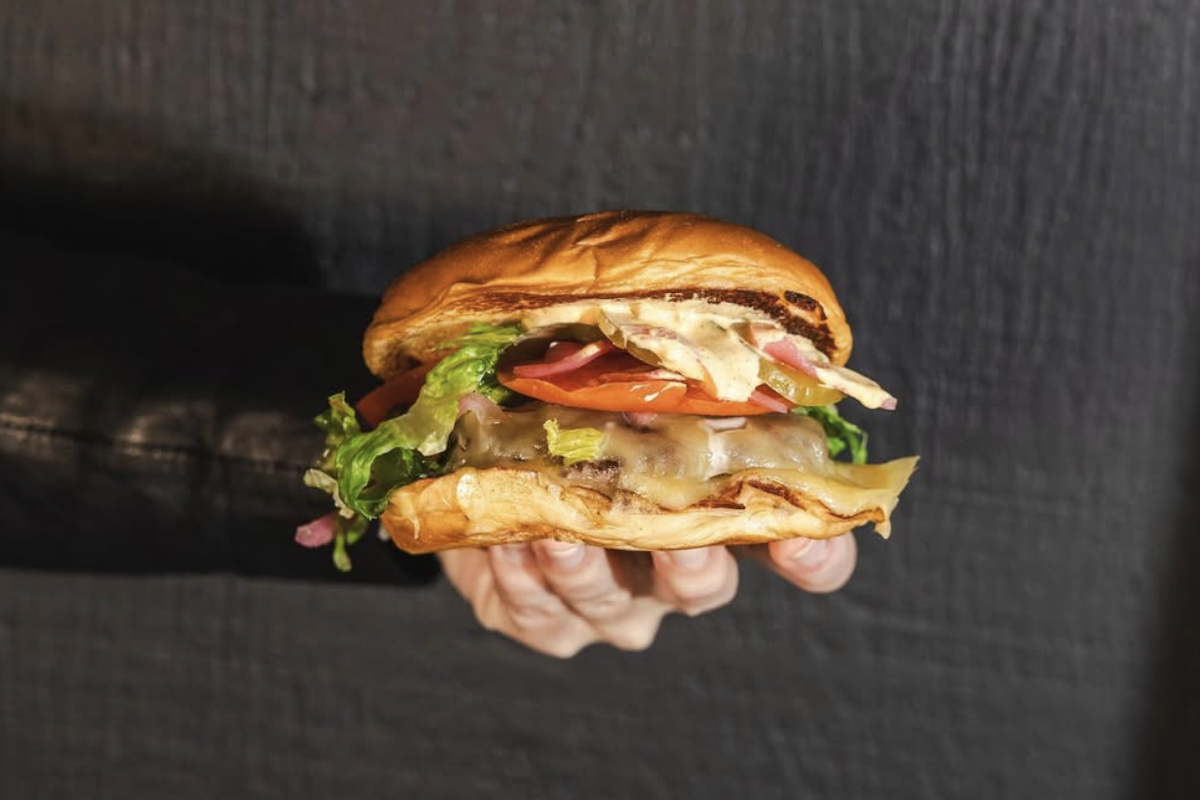 A smashburger with many toppings including cheese, tomato and lettuce.