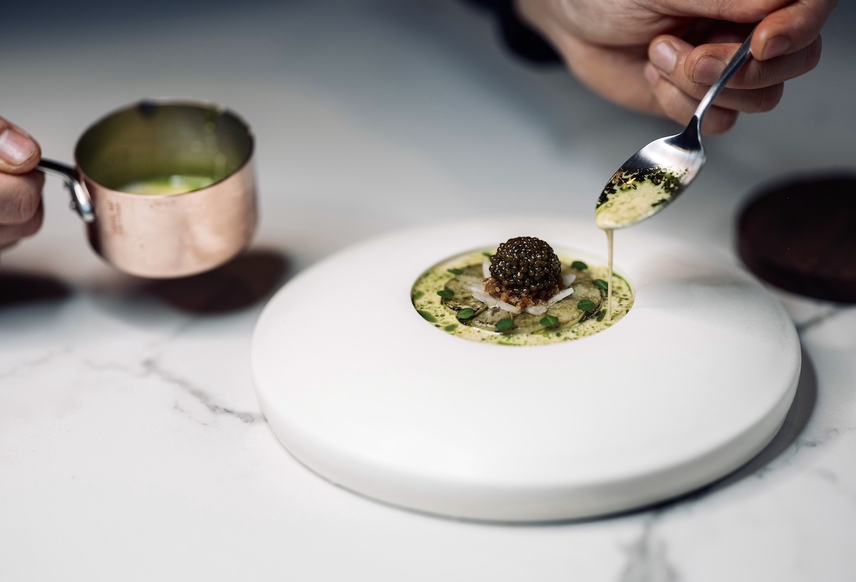 A white plate with a soup in the middle, garnished with fancy toppings.