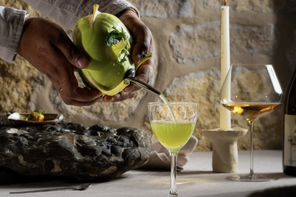 Someone pours a bright green drink into a wine glass.