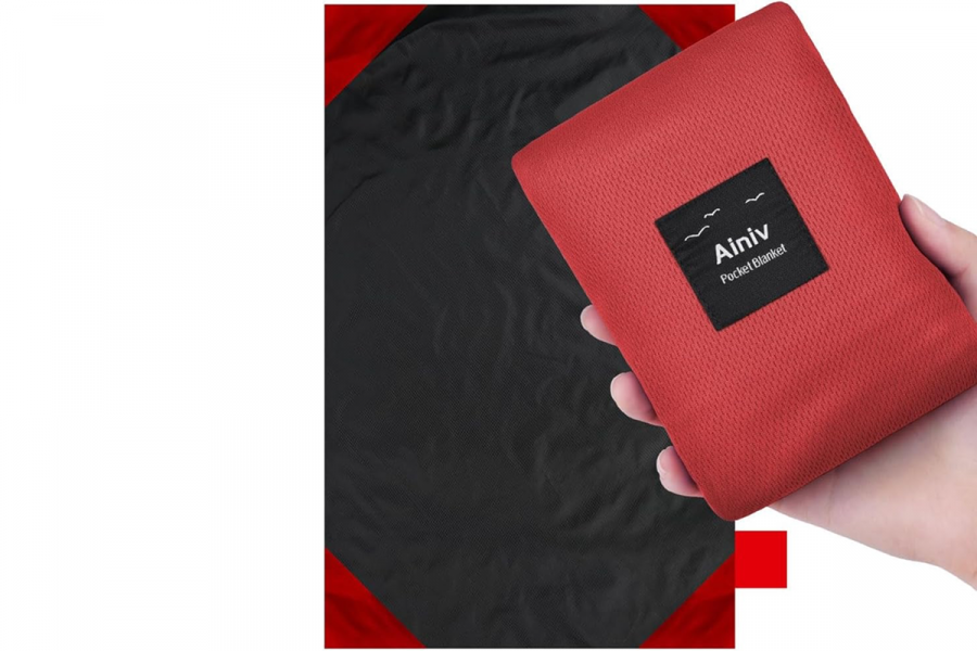Ainiv A red and black rectangle blanket is behind a hand, holding a small red bag with the word Aniviv printed on it.