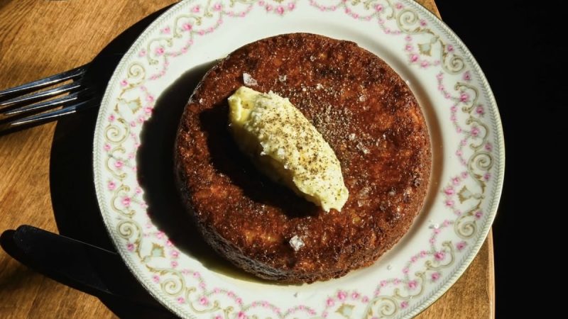 Hatchet Hall-Los Angeles-@hatchethall Golden-brown cornbread served on a vintage floral plate, topped with a generous scoop of whipped butter and a sprinkle of black pepper and sea salt.