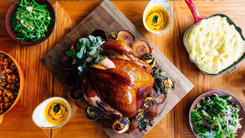 A beautifully cooked Thanksgiving turkey is placed on a wooden cutting board on a table surrounded by various side dishes, including mashed potatoes, green beans, stuffing, and a fresh salad. The table is set for a festive meal.