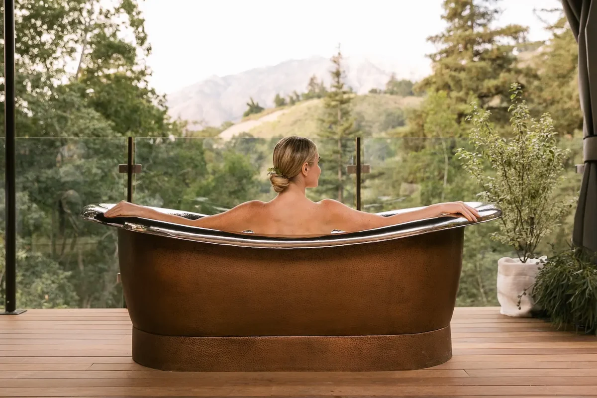 Woman sits in spa bathtub overlooking the hills of Monterey Peninsula from her hotel room at Ventana in Big Sur, California